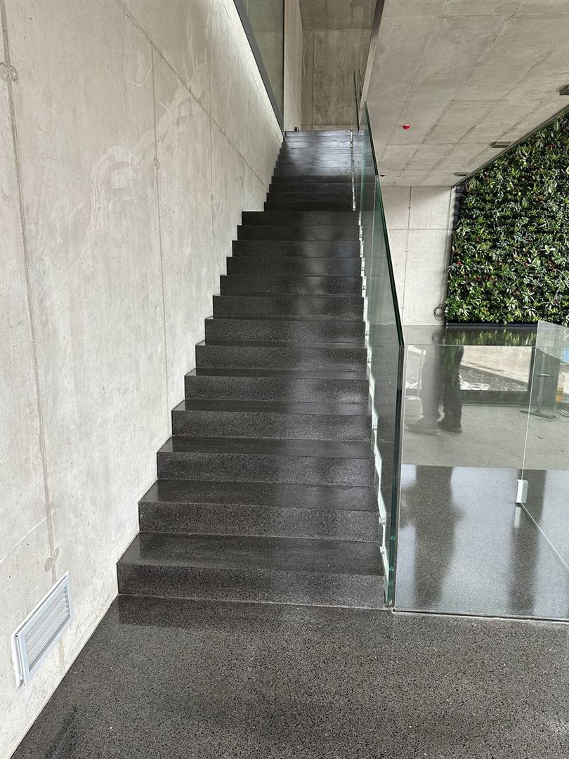 Detail von Glasbrüstung und Handlauf neben heller Terrazzotreppe