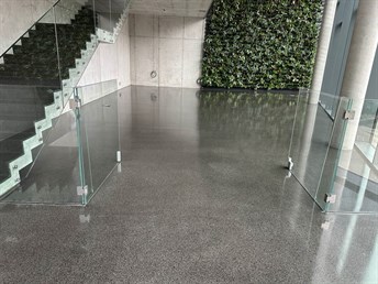 Vstupní hala s tmavou leštěnou litou terrazzo podlahou a skleněným zábradlím