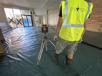 Pracovník s laserovým přístrojem měří výšku anhydritové podlahy