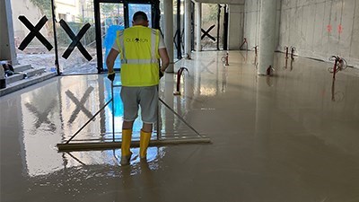 Pracovník vyrovnává čerstvě litý anhydritový potěr v prosklené hale