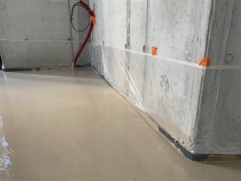 Rovný povrch čerstvého anhydritového potěru u betonové stěny